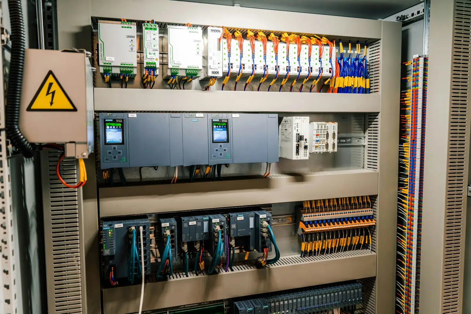 An open control cabinet: programmable logic controller (PLC) CPUs, power supplies, network switches and rows of terminal blocks.