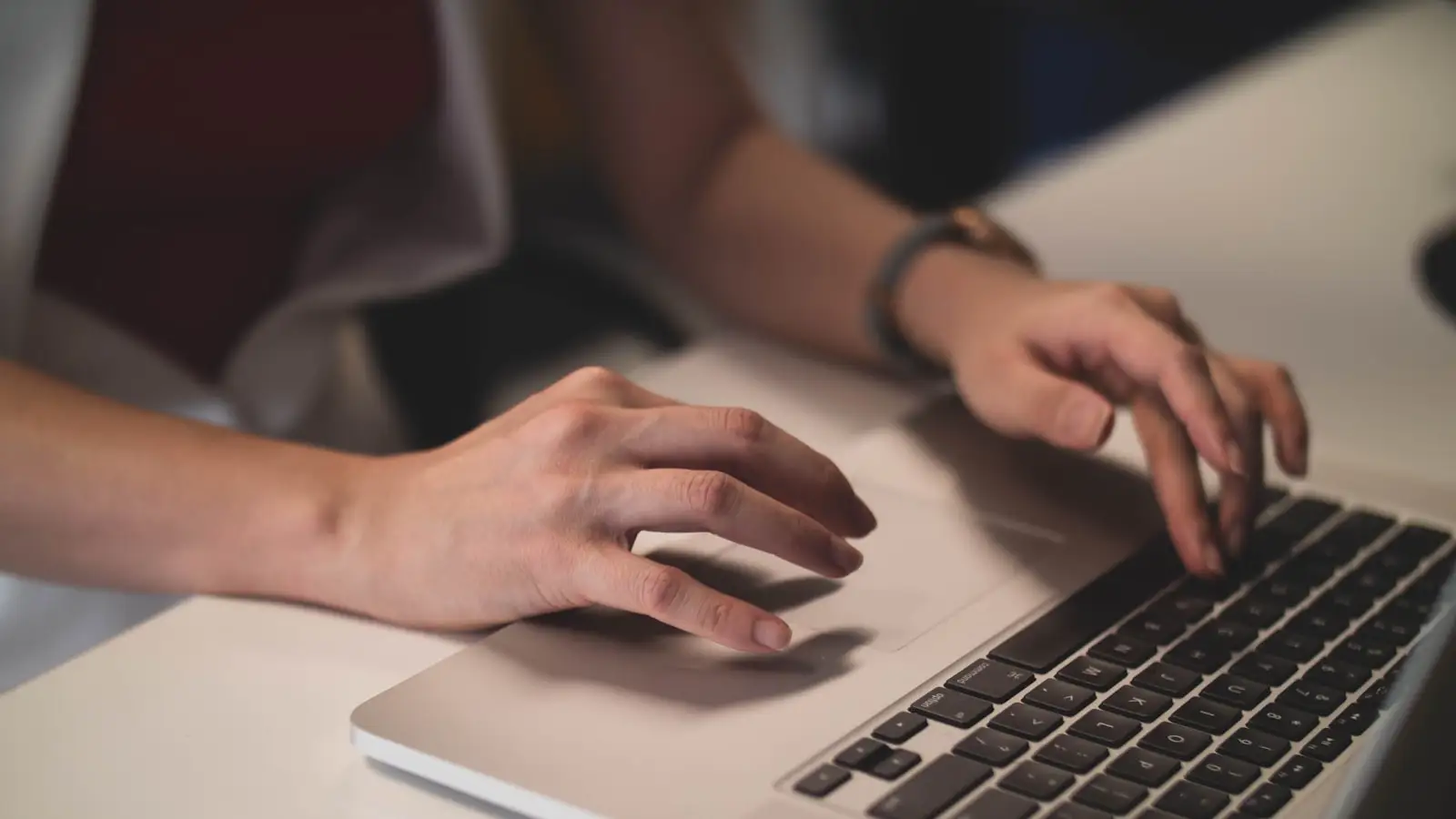 Two hands on a laptop keyboard at a clean desk.