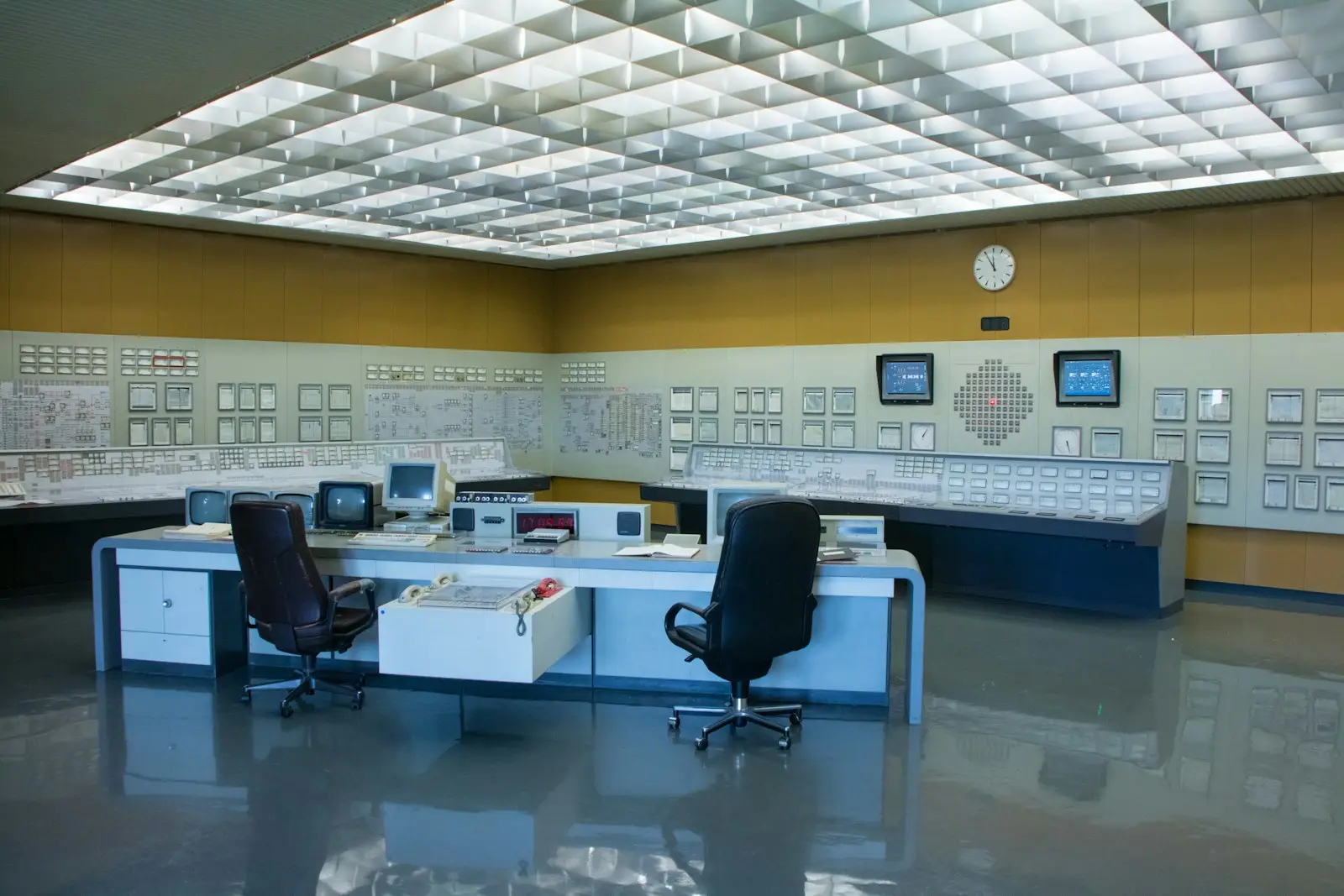 A control room console with open logbooks and a wall of instrument panels