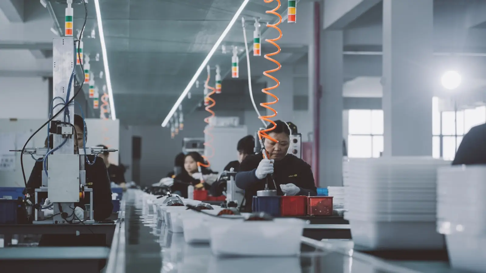 Three workers assembling parts at a bench line with pneumatic tools