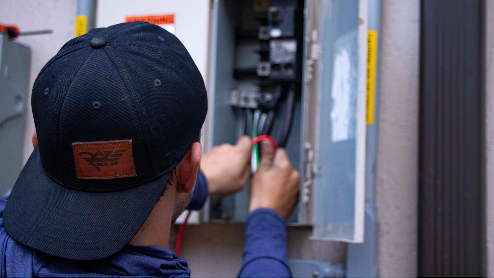 A technician working inside an open electrical panel.
